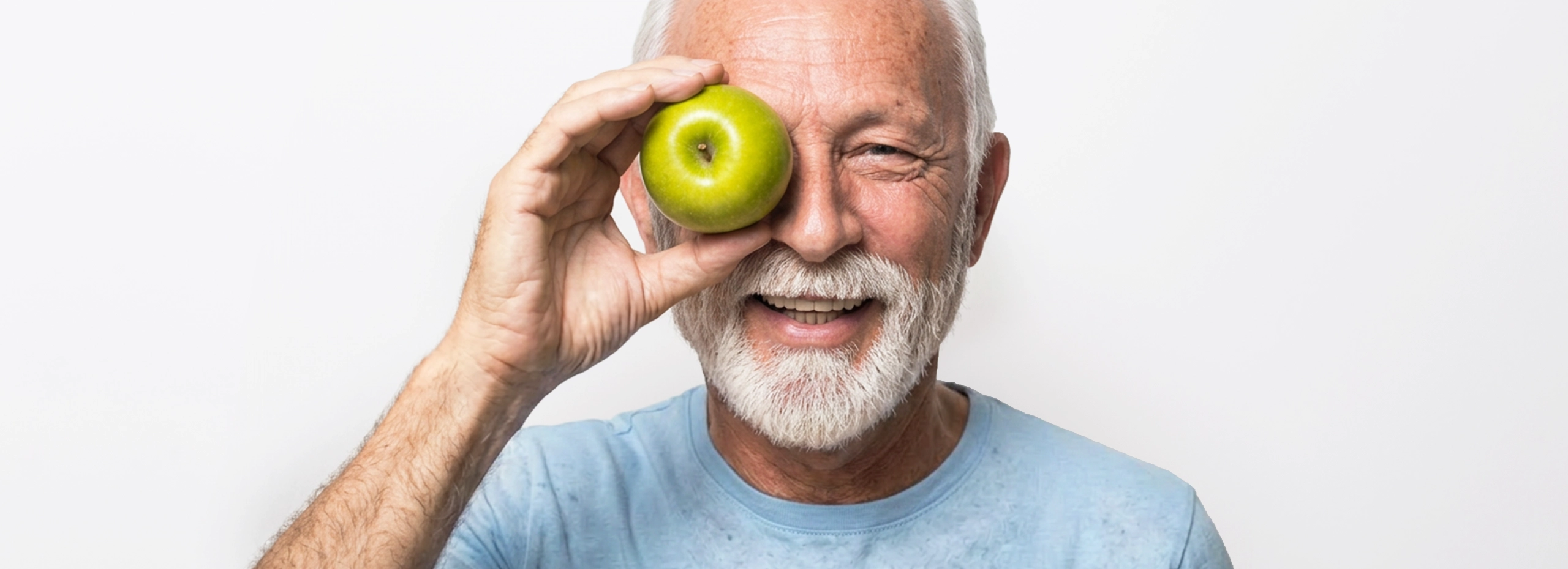 Älterer Mann hält einen grünen Apfel vor sein Auge